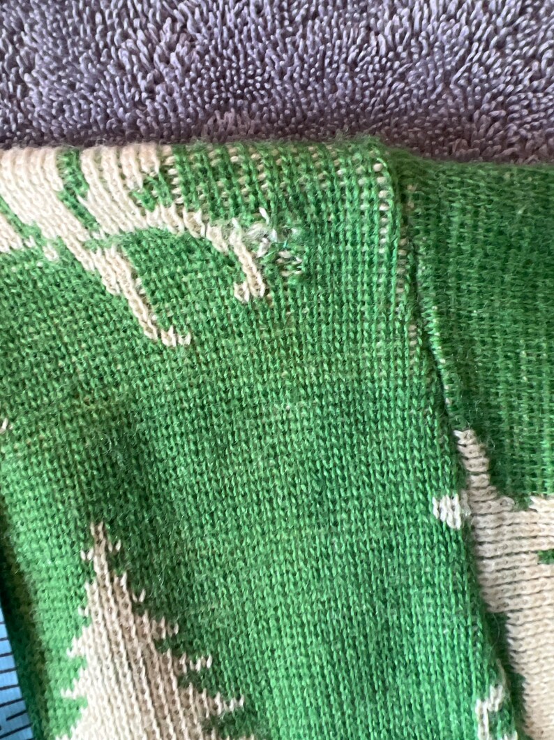 May include: Close-up of a green and white knitted sweater with a pattern of trees. The sweater is made of a soft, comfortable material.