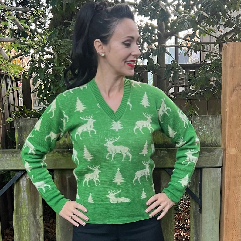 May include: A green sweater with a white reindeer and pine tree pattern. The sweater has a v-neck and long sleeves.