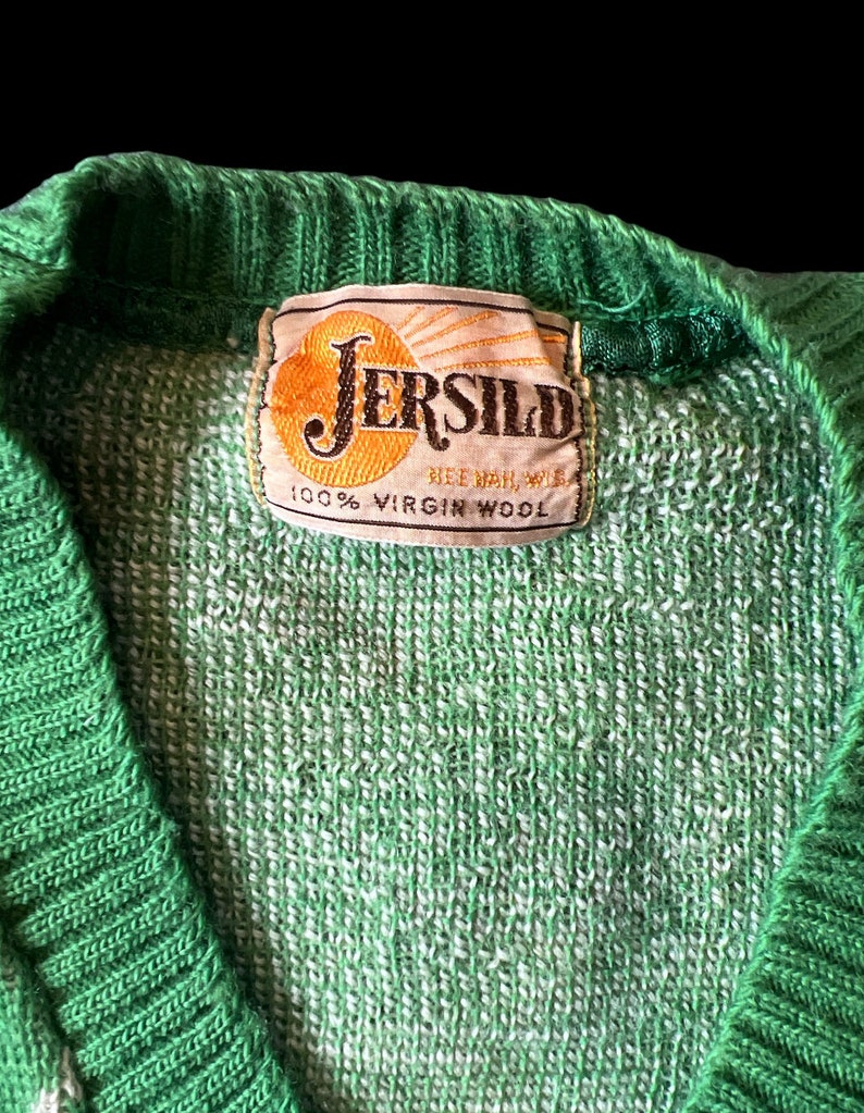 May include: A green and white knit sweater with a label that reads "Jersild 100% Virgin Wool".
