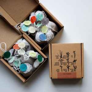 Könnte beinhalten: Drei Kartons mit einer Auswahl an kleinen, weißen Stoffbeuteln, die mit Samen gefüllt sind. Die Beutel sind mit verschiedenen Namen von Gemüse und Kräutern in schwarzer Schrift auf bunten Kreisen beschriftet. Die Kartons sind mit "BIO ZIARNA" in schwarzer Schrift auf braunem Hintergrund beschriftet.