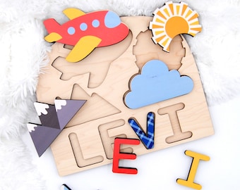 May include: Wooden puzzle with a red airplane, blue cloud, yellow sun, gray mountains, and the name "LEVI" in blue, red, and yellow letters. The puzzle pieces are separate from the board.