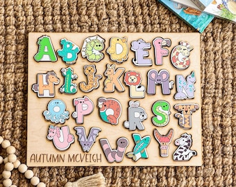 May include: Wooden alphabet puzzle with animal illustrations. Each letter is a different color and features a unique animal design. The puzzle is labeled "AUTUMN MCVEIGH".