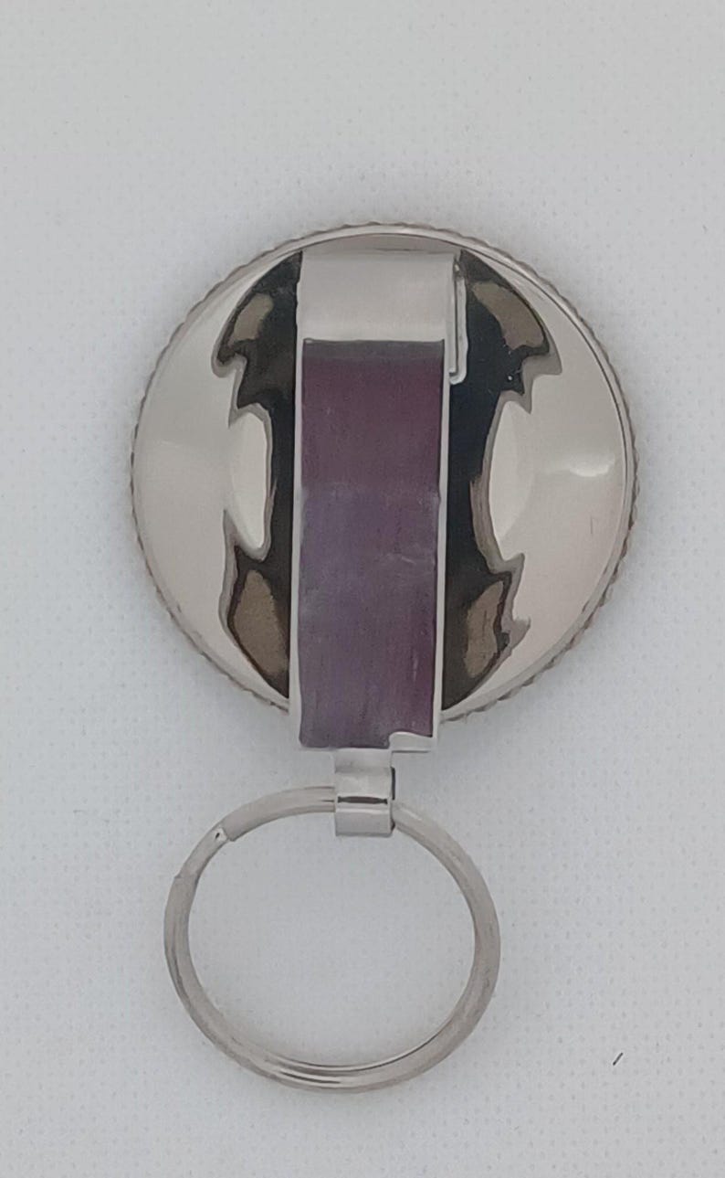 Puede incluir: Llavero plateado con un dije redondo de metal plateado y un anillo plateado. El dije tiene una superficie texturizada y estampada.