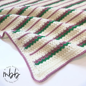 May include: A white crocheted baby blanket with pink and green stripes. The blanket has a pink border and is folded in half.