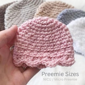 May include: A close-up of a pink crocheted baby hat with a scalloped edge, held in a hand. Several other crocheted hats in various neutral colors are visible in the background. The text "Preemie Sizes" and "NICU / Micro Preemie" is at the bottom.