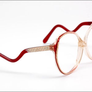May include: Red and clear plastic eyeglasses with a unique, curved frame design.