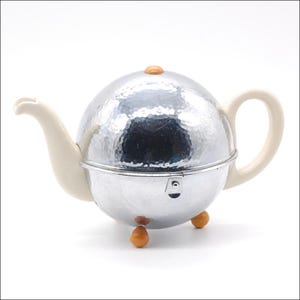 May include: A silver-colored teapot with a hammered texture, cream-colored handle and spout, and small wooden-colored feet. The teapot has a round shape with a lid and a small wooden-colored knob on top. A unique tea accessory.