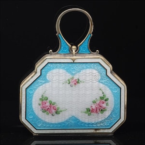 May include: An antique silver-toned handbag with a light blue enamel border and handle. The center features a white design with pink roses and green leaves. The handle and accents are silver-toned.