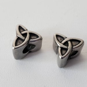 May include: Two silver metal charms in the shape of a Celtic knot, also known as a trinity knot. The charms are three-dimensional and have a smooth, polished finish.
