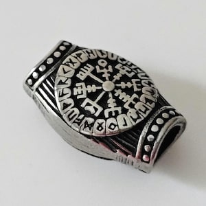 May include: A silver-toned metal bead with a circular design featuring a compass rose and runes. The bead has a hole for threading.