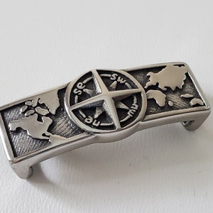 May include: A silver metal belt buckle with a compass and a world map design.