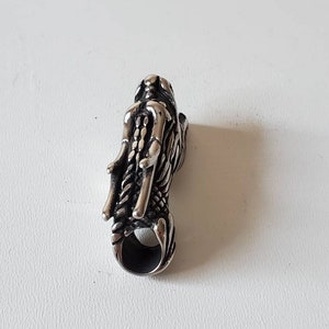 May include: A silver-colored dragon pendant with intricate details. The pendant features a dragon head with detailed scales and a loop at the bottom for a chain. The dragon's design is highly detailed and textured.