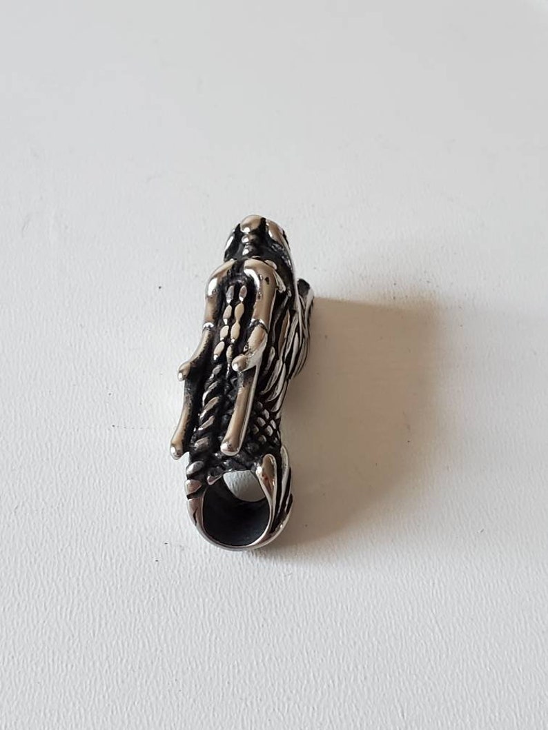 May include: A silver-colored dragon pendant with intricate details. The pendant features a dragon head with detailed scales and a loop at the bottom for a chain. The dragon's design is highly detailed and textured.