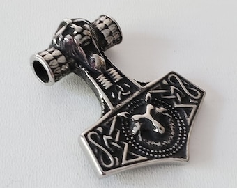 May include: A silver-coloured pendant in the shape of Thor's hammer, Mjolnir. The hammer features intricate detailing, including a textured handle and Celtic knotwork on the head. The pendant is designed to be worn as a necklace.