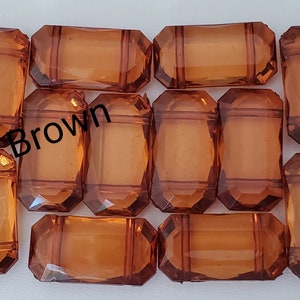 May include: Twelve brown, faceted, rectangular glass beads. The beads have a slightly translucent quality.