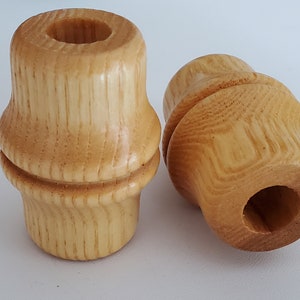 May include: Two wooden finials with a light brown color and a smooth, rounded surface. The finials have a hole in the center and a groove around the middle.