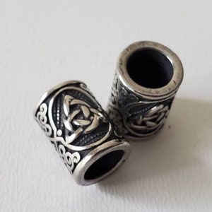 May include: Two silver-toned metal beads with a Celtic knot design. The beads are cylindrical and have a smooth, polished finish.