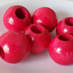 May include: Six bright red wooden beads with a hole through the center. The beads are round and smooth.