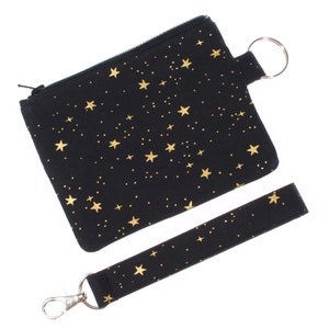 May include: A black zippered pouch with a gold star pattern and a matching black wrist strap with a gold star pattern. The pouch has a silver zipper and a silver key ring.