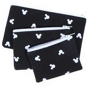 May include: Three black zippered pouches with white Mickey Mouse silhouettes printed on them. The pouches are nested inside each other, with the largest pouch on the bottom and the smallest pouch on top.