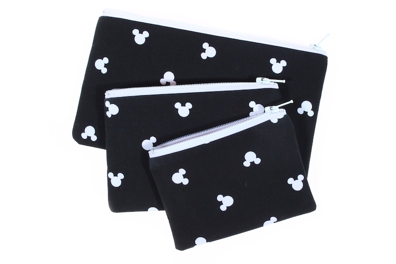 May include: Three black zippered pouches with white Mickey Mouse silhouettes printed on them. The pouches are nested inside each other, with the largest pouch on the bottom and the smallest pouch on top.