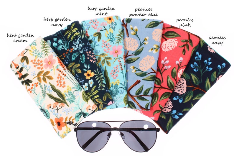 May include: Assortment of fabric eyeglass cases with floral patterns. The cases are in various colors, including cream, navy, mint, powder blue, pink, and navy. The text on the cases reads "herb garden" and "peonies".