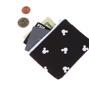 May include: A black zippered pouch with a white Mickey Mouse pattern. The pouch is open and has a credit card, a debit card, and a dollar bill inside.