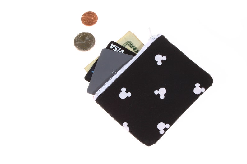 May include: A black zippered pouch with a white Mickey Mouse pattern. The pouch is open and has a credit card, a debit card, and a dollar bill inside.