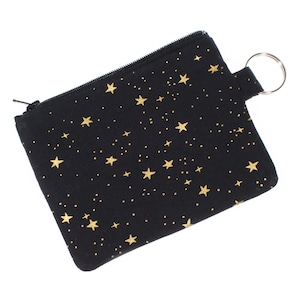 May include: A black zippered pouch with a gold star pattern and a silver key ring.