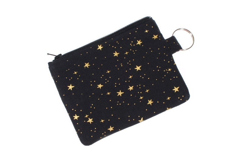 May include: A black zippered pouch with a gold star pattern and a silver key ring.