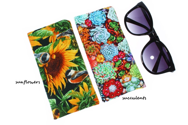 May include: Two fabric eyeglass cases with different floral patterns. One case features a sunflower design with birds, and the other case features a succulent design. Both cases are black with a white background.