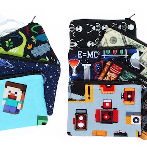 May include: A stack of nine zippered pouches with various colorful patterns. The pouches feature designs such as dinosaurs, skeletons, books, cameras, and Minecraft characters.