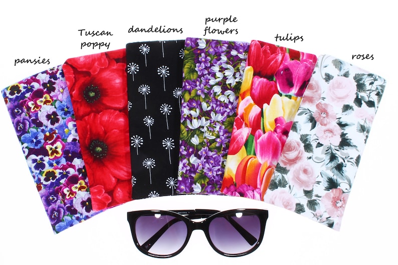 May include: Six different floral patterned eyeglass cases, each with a different flower design. The cases are arranged in a semi-circle with a pair of black sunglasses in the center. The cases are labeled with the names of the flowers: pansies, Tuscan poppy, dandelions, purple flowers, tulips, and roses.