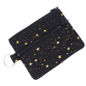May include: A black zippered pouch with a gold star pattern. The pouch has a small ring attached to it.