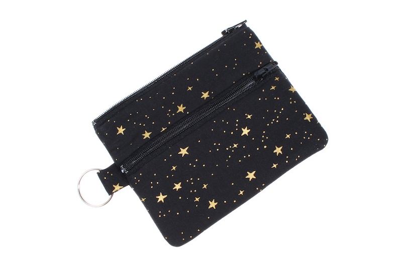 May include: A black zippered pouch with a gold star pattern. The pouch has a small ring attached to it.