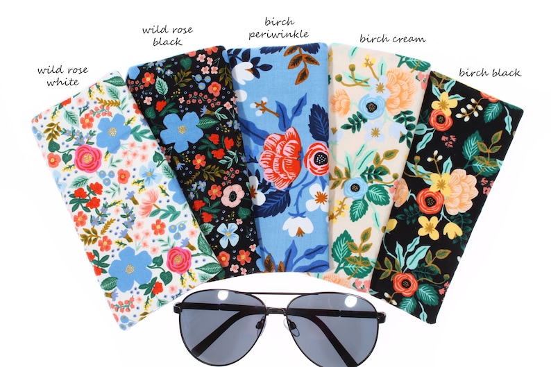 May include: Five different floral patterned eyeglass cases, each with a different color background: white, black, blue, cream, and black. The cases are arranged in a semi-circle with a pair of black sunglasses in the center.