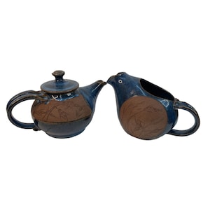 May include: A blue and brown ceramic teapot and creamer set with a leaf design. The teapot has a lid and a spout. The creamer has a handle and a spout.