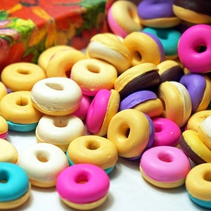 May include: A collection of colorful mini donuts with various glazes and sprinkles. The donuts are arranged in a pile on a white surface.
