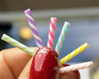 May include: A close-up of six colorful striped paper straws, held in a hand with red nail polish. The straws are in various colors, including pink, yellow, green, blue, and purple.