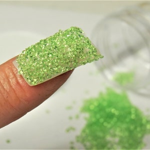 May include: A fingernail with a green glitter nail polish. The glitter is small and densely packed, creating a sparkling effect.