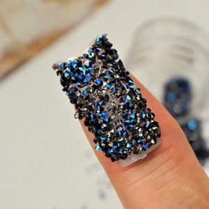 May include: A fingernail with a design of iridescent blue and black rhinestones.