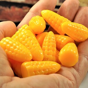 May include: A handful of small, bright yellow corn-shaped candies. The candies have a textured surface, resembling corn kernels. The image is a close-up shot, highlighting the vibrant color and shape of the treats. The background is blurred.