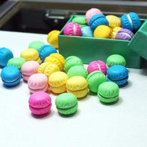 May include: A collection of colorful macarons in a green box. The macarons are in various shades of pink, blue, green, and yellow.