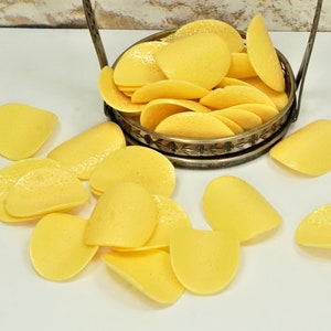 May include: A bowl filled with yellow potato chips, with additional chips scattered around the bowl on a white surface.