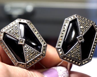 May include: A pair of vintage cufflinks with a geometric design. Each cufflink features a black onyx center framed by a silver-toned metal with marcasite accents. The cufflinks have a rectangular shape with a central square detail.
