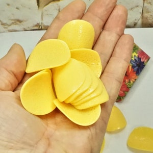 May include: A hand holding a pile of yellow potato chips. The chips are arranged in a flower shape.