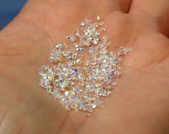 May include: A close-up of a hand holding a pile of iridescent clear rhinestones.