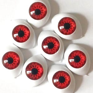 May include: A collection of eight doll eyes with a striking red iris and a black pupil. The eyes are set in a white, oval-shaped base, creating a dramatic and intense appearance. These craft supplies are ideal for doll making or other creative projects.