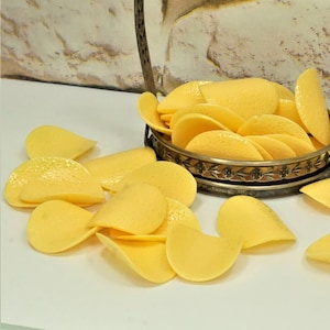 May include: A silver serving dish filled with yellow plastic chips. The chips are arranged in a decorative pattern and are spilling out of the dish onto a white surface.