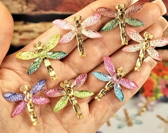 May include: Assortment of colorful dragonfly embellishments with gold accents. Each dragonfly has a sparkly finish and is perfect for adding a touch of whimsy to crafts and jewelry.